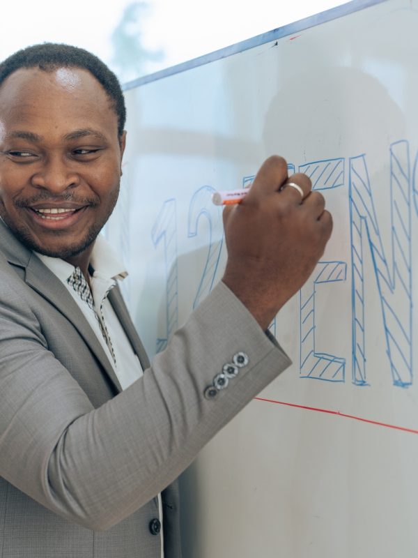 African senior male calculus professor is writing on whiteboard in the classroom