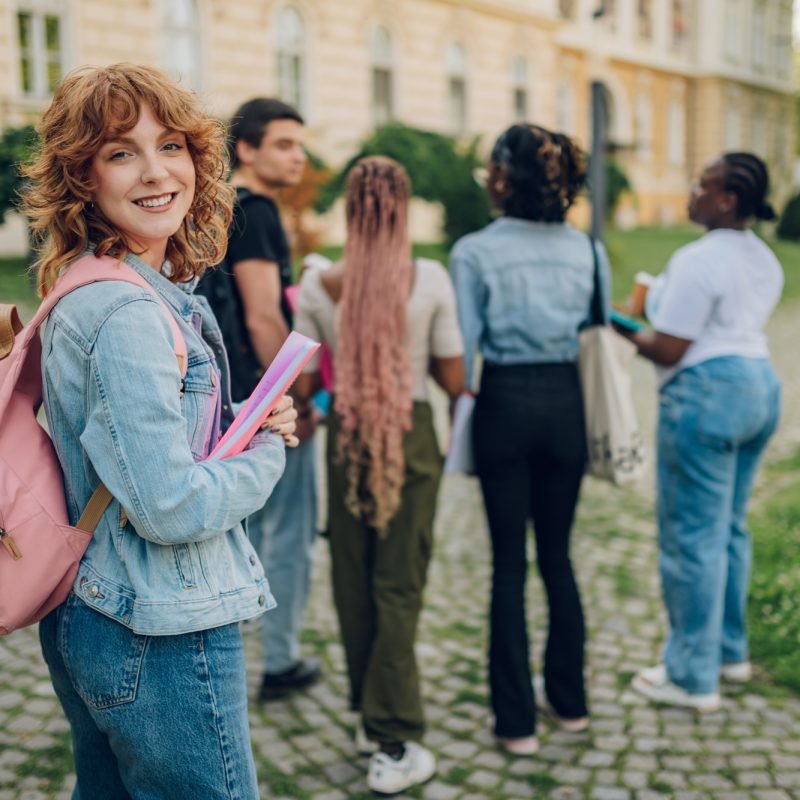 Portrait of happy student with textbook and backpack at campus.